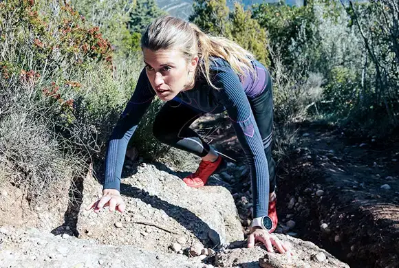 Female athlete climbing a rugged terrain during an outdoor endurance challenge.