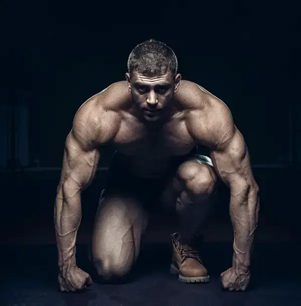 Muscular athlete crouched in a starting position, highlighting physical fitness and strength.