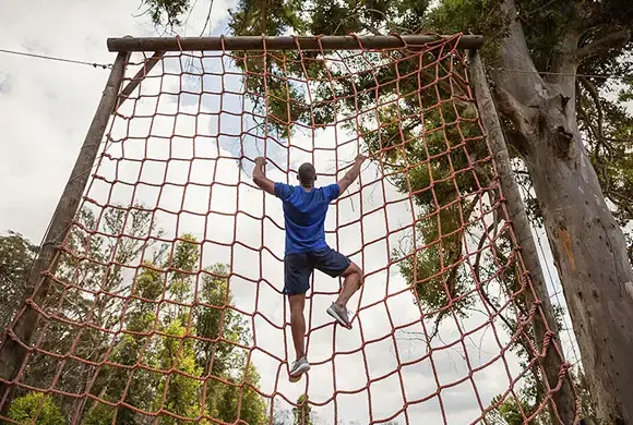 Athlete climbing a net obstacle during a race, demonstrating agility and strength.